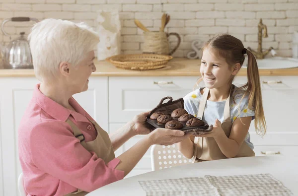 Souriante fille et sa mamie tenant plateau avec des muffins au chocolat frais à la maison — Photo