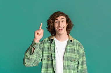 Creative idea. Happy millennial guy showing EUREKA gesture on turquoise background