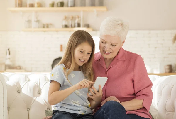 Mature woman playing video games on smartphone with her granddaughter at home — Stock Photo, Image