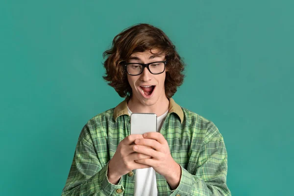 Victory and success. Shocked millennial guy with mobile phone screaming OMG on color background — Stockfoto