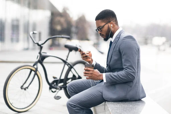 Hombre de negocios negro en auriculares mensajes de texto en el teléfono beber té — Foto de Stock