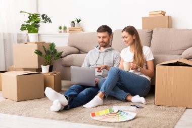 Happy young couple searching samples of interiors on laptop
