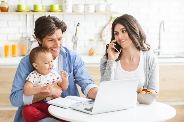 Millennial parents with baby son working on laptop at kitchen — Stock Photo, Image