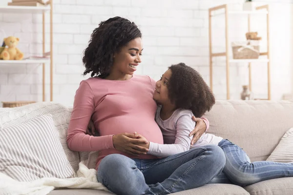 Cute little black girl and her pregnant mom embracing at home — Stok fotoğraf