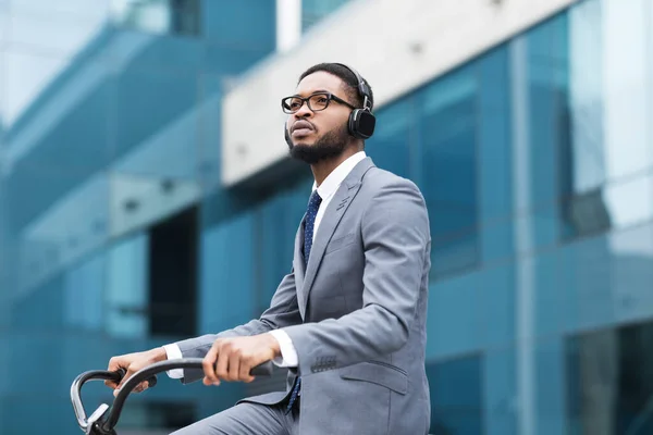 Afro businessman in earphones riding on bike — стокове фото