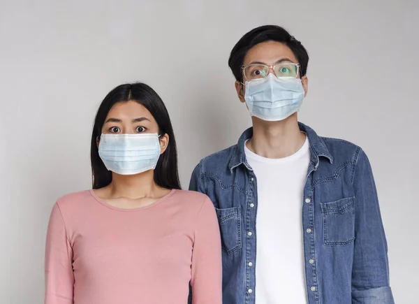 Coronavirus Concept. Frightened asian couple posing in protective medical masks — Stockfoto