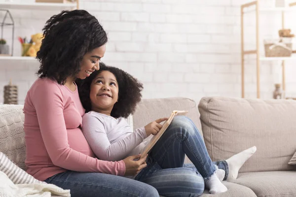 Little Black Girl Reading Book With Her Pregnant Mom At Home — Stok fotoğraf