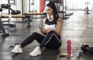 Spor kulübünde cep telefonu ve kulaklığı olan genç bir bayan.