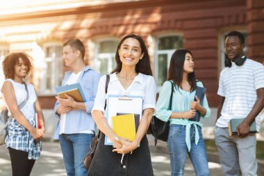 Üniversite kampüsünde elinde notlarla poz veren mutlu Arap öğrenci kız.