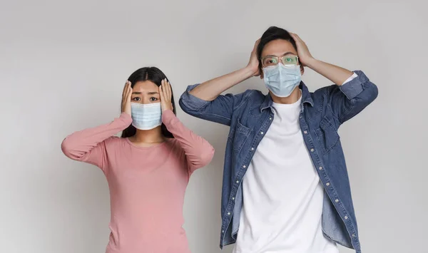 Coronavirus Paniek. Aziatisch paar in beschermende maskers met bang gezicht expressie — Stockfoto