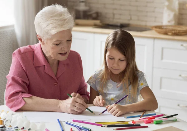 Happy mature lady with her granddaughter drawing together in kitchen — Stock Photo, Image