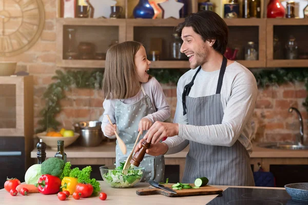 Feliz padre y pequeña hija cocinando ensalada de verduras en la cocina — Foto de Stock