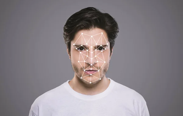 Biometrische identificatie. jong mannetje kijken naar camera met veelhoekige mesh op zijn gezicht tegen grijze achtergrond — Stockfoto