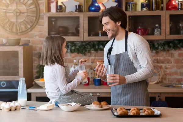 Веселый отец и дочь едят печенье и пьют молоко на кухне — стоковое фото