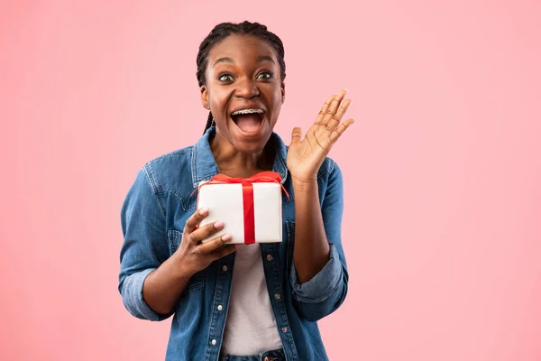 Vreugdevol Afrikaans meisje schreeuwen Holding Gift poseren op roze achtergrond — Stockfoto