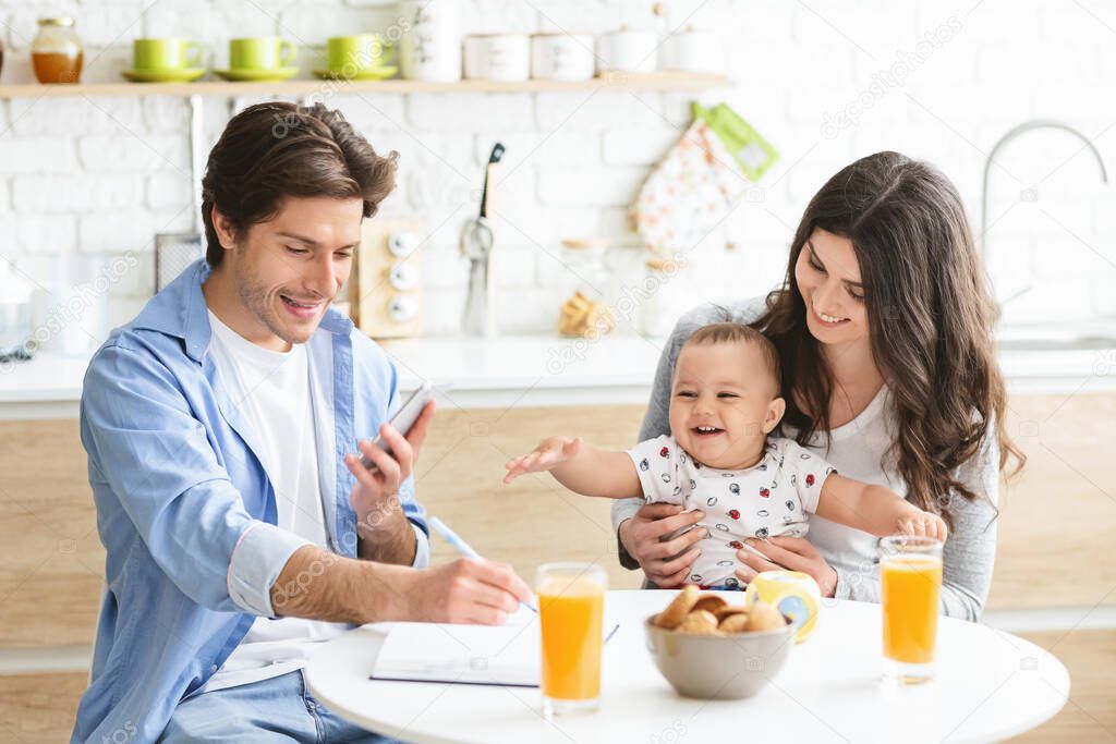 Young man texting on cellphone, dining with his wife and baby