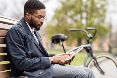 Parkta dijital tablet üzerinde çalışan yakışıklı yönetici