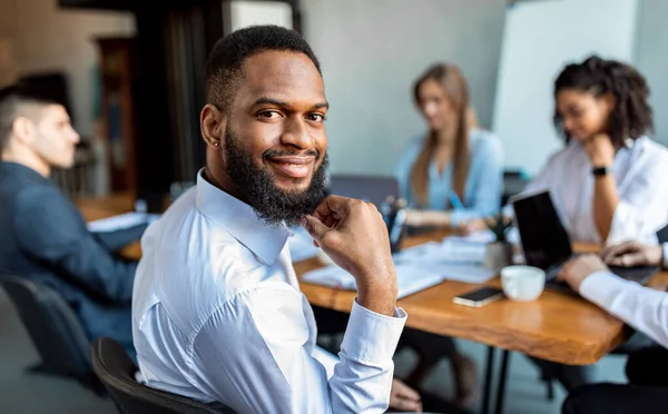 Empresário afro-americano sentado sorrindo para a câmera no escritório moderno — Fotografia de Stock