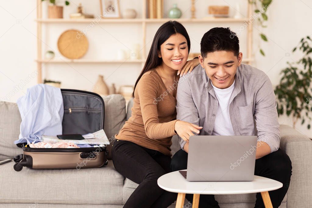 Smiling Asian Couple Using Laptop Booking Vacation Tour At Home