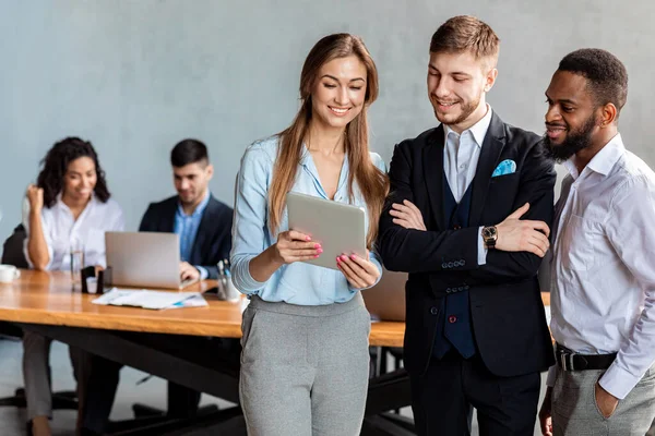 Compañeros de trabajo sosteniendo tableta digital discutiendo noticias de negocios de pie en la oficina — Foto de Stock