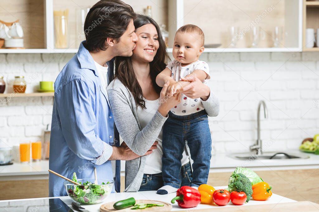 Young parents embracing with baby son at kitchen