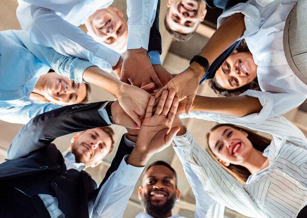 Coworkers Standing In Circle Holding Hands During Meeting In Office