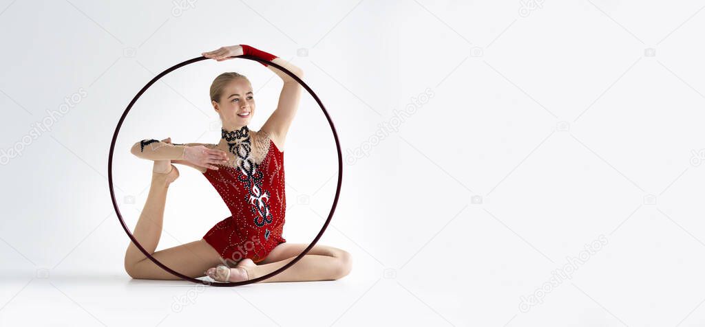 Female athlete doing complicated gymnastic exercise with hoop on white background, panorama with empty space