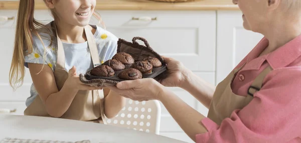 Felismerhetetlen érett hölgy és unokája tálca frissen sült muffinnal a konyhában, közelkép — Stock Fotó