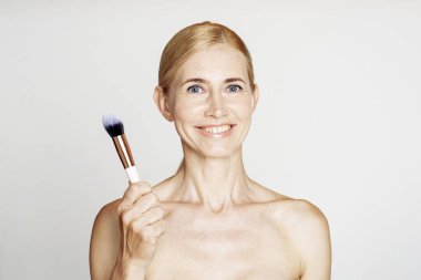 Güzel olgun bir kadın stüdyoda fırça tutuyor.