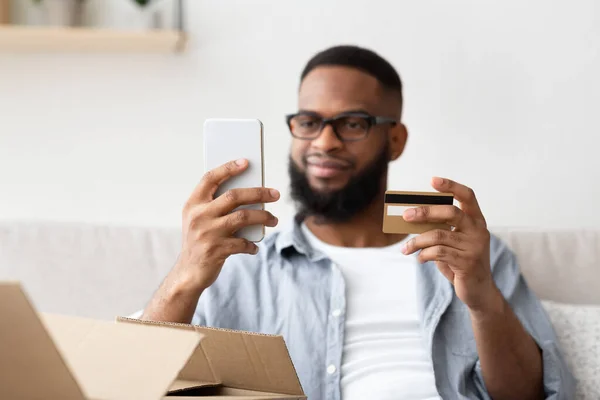 Chico afroamericano con teléfono inteligente y tarjeta de crédito hace la compra —  Fotos de Stock