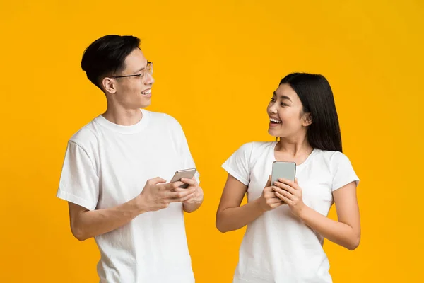 Heureux asiatique couple regarder l 'autre tout en utilisant smartphones — Photo