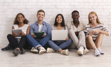 Beyaz tuğla duvarın üzerinde çalışan gülümseyen bir grup uluslararası öğrenci