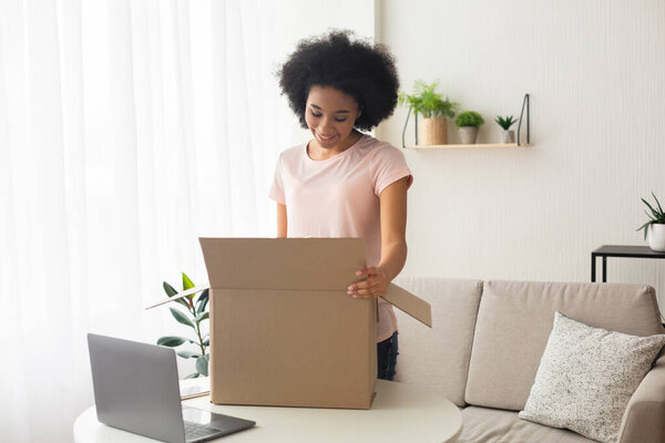 Smiling african american woman, near box and laptop