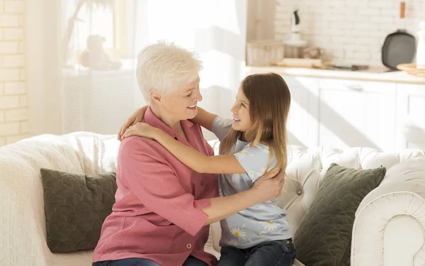 Little child and her grandmother hugging each other on sofa — Stock Photo, Image