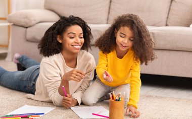 Mutlu anne ve kızı evde yerde yatarken çiziyor.