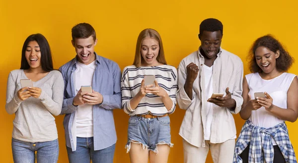 Amigos adolescentes emocionales que se quedan en fila, usando teléfonos móviles —  Fotos de Stock