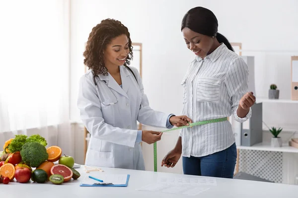 Giovane signora nera in visita moderna dietologa, prendendo misure — Foto Stock