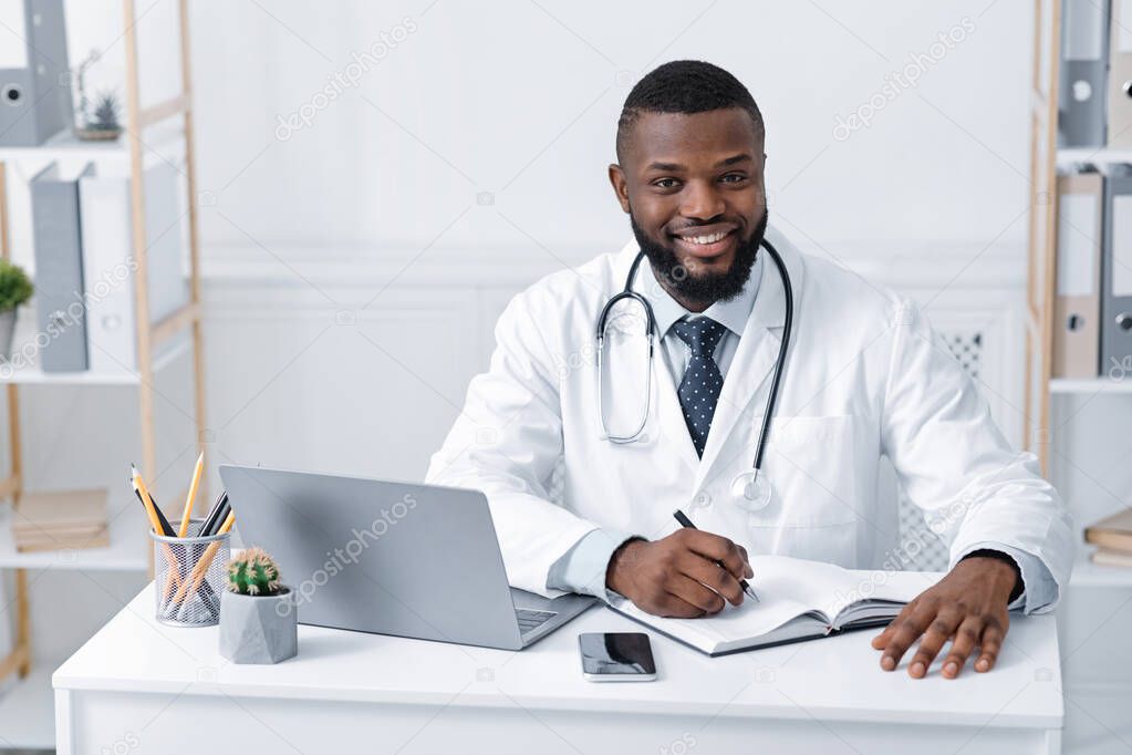 Smiling black doctor working with laptop in office