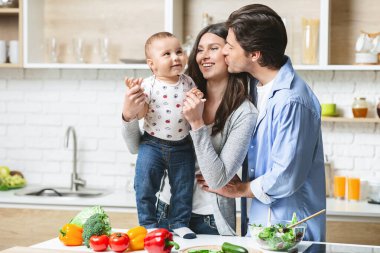 Mutfakta bebeğe sarılan genç aile, boş bir alan.