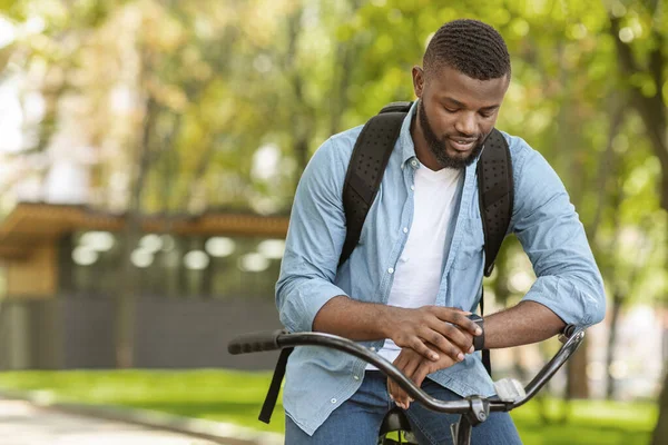 Rastreador de Fitness. Bonito homem africano de bicicleta olhando para seu Smartwatch — Fotografia de Stock