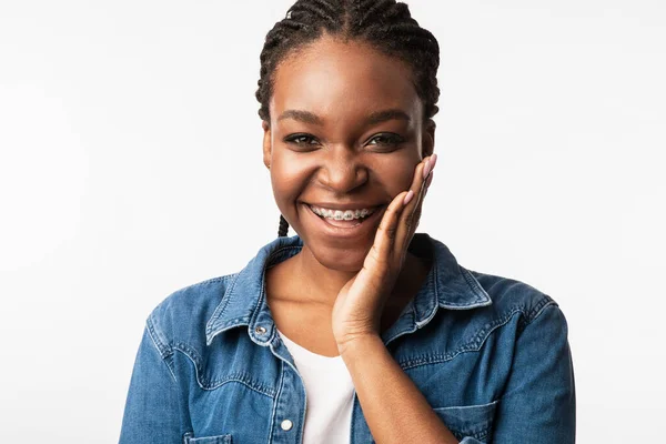 Menina africana feliz com aparelho tocando rosto posando no estúdio — Fotografia de Stock