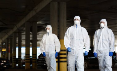 Virüs korumalı giysiler içindeki doktorlar halka açık otoparkta görevdeler.