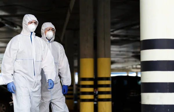 Hombres con trajes de protección contra el virus patrullan la ciudad en cuarentena — Foto de Stock