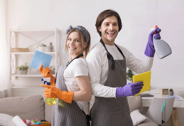 Profesionales de limpieza. Alegre pareja milenaria sosteniendo aerosoles de detergente y trapos —  Fotos de Stock