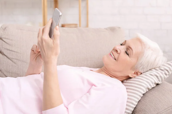 Seniorin liest Nachrichten auf Handy und ruht sich zu Hause aus — Stockfoto