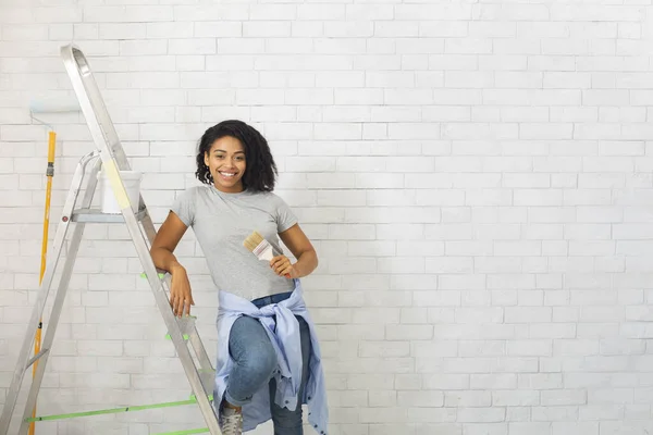 Female leans on stepladder with brush in hand — Stock Photo, Image