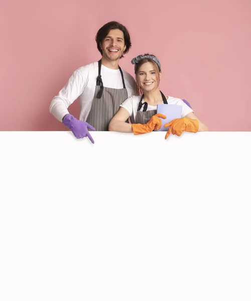 Mosolygó pár visel tisztító kesztyű és rámutatva a fehér hirdetési fórumon — Stock Fotó