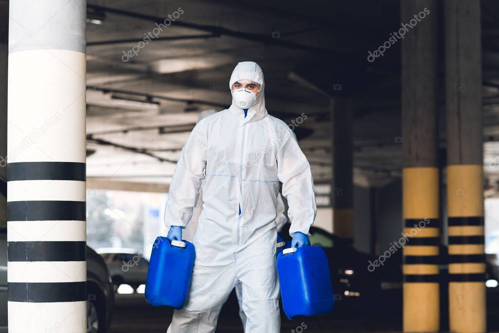 Man in virus protective suit holding two jerrycans with antiseptic