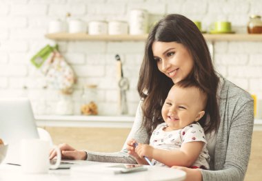 Ev mutfağında dizüstü bilgisayarla çalışan neşeli bir anne.
