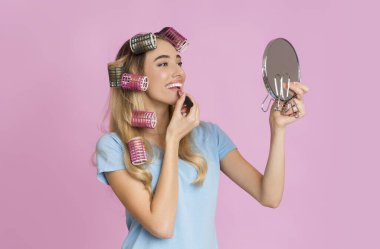 Housewife paints her lips and looks in mirror clipart